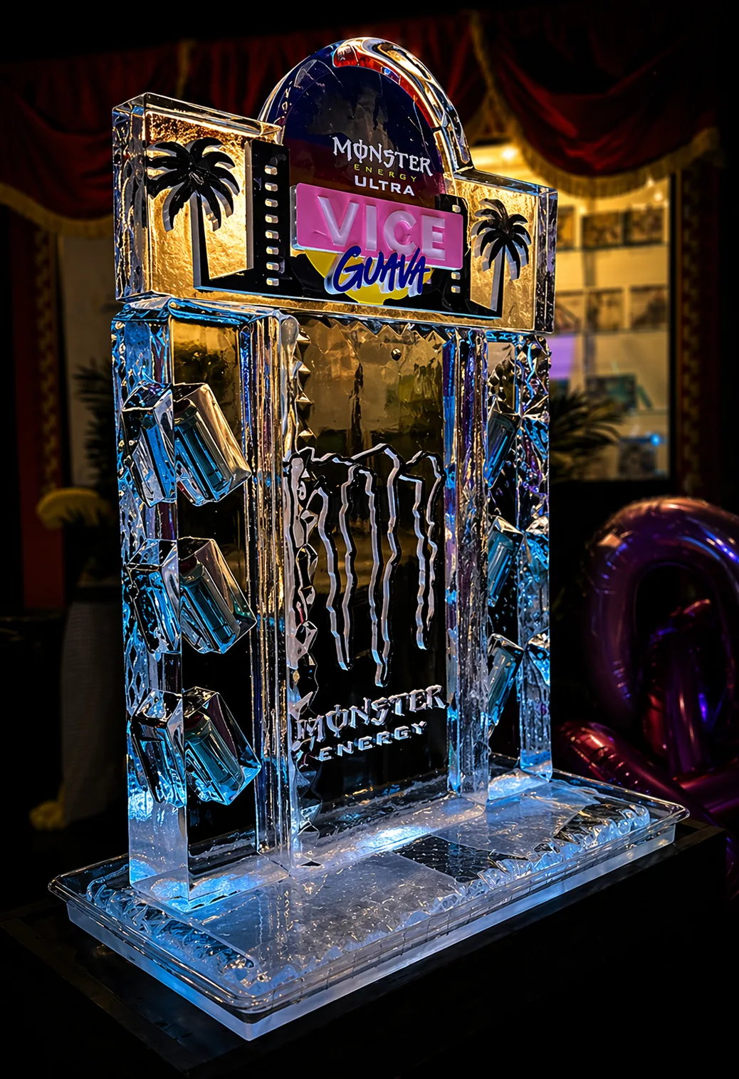 Clear ice bar structure engraved with Monster Energy claw logo and MONSTER ENERGY text, topped with a colorful VICE Guava sign flanked by palm tree carvings.