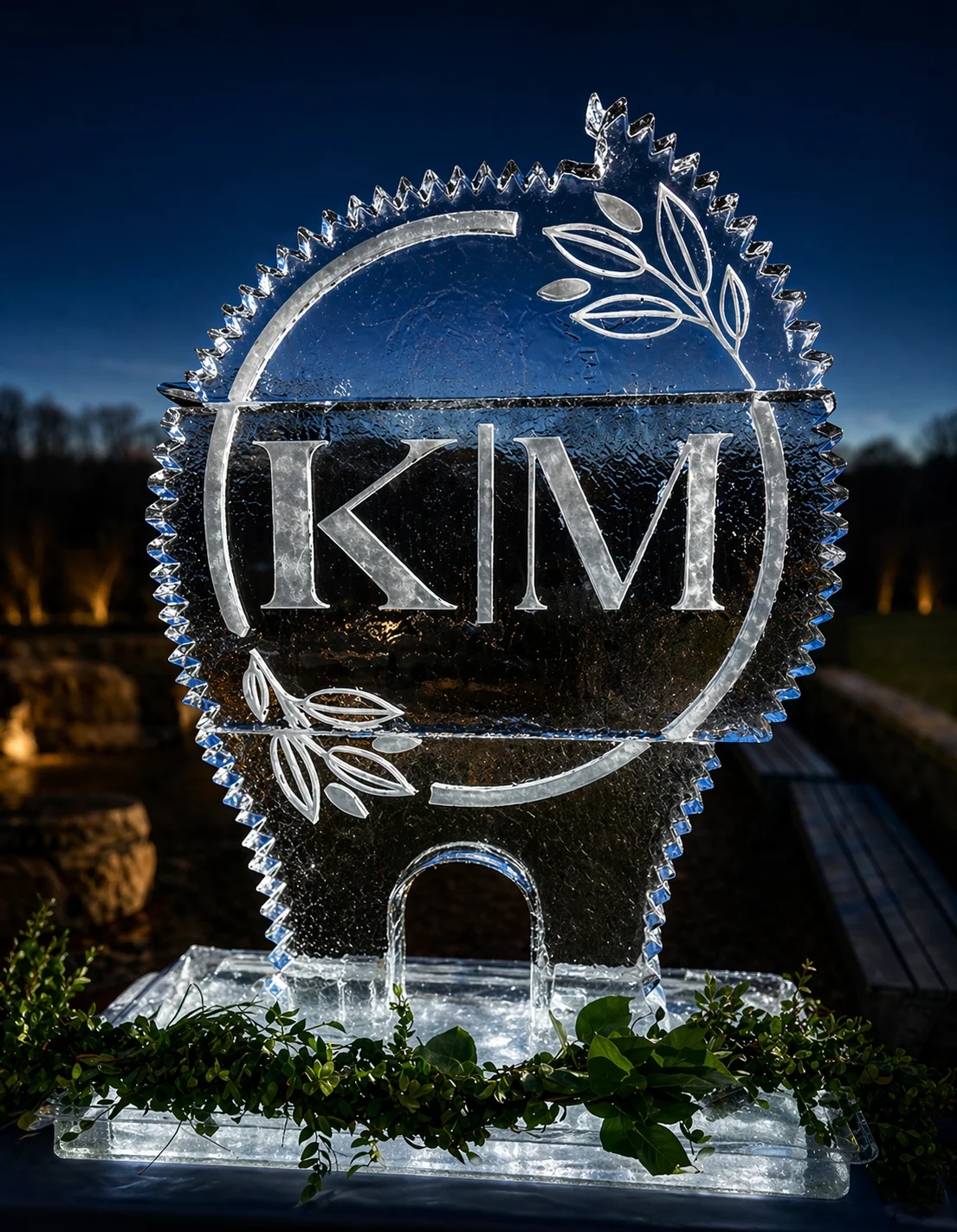 KLM monogram ice sculpture with leafy greenery at an outdoor evening event.