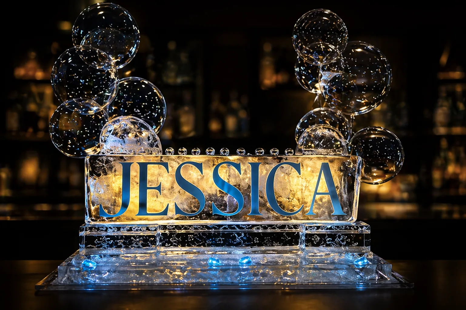 Clear ice sculpture carved with the name Jessica in script lettering, lit from below at an evening celebration.